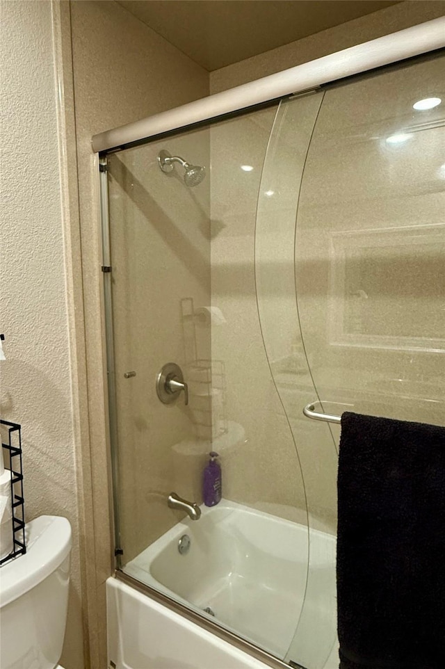 bathroom featuring toilet and bath / shower combo with glass door