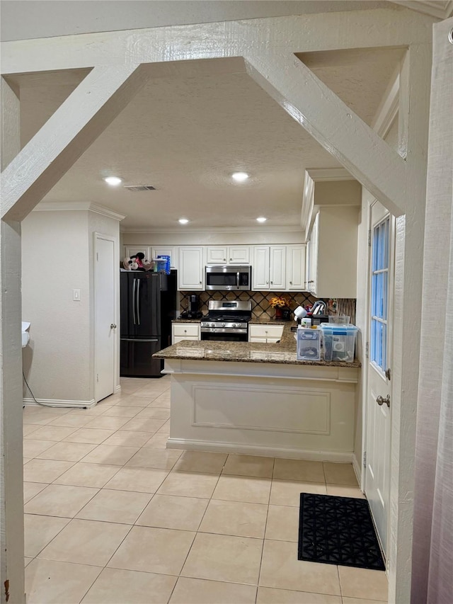 kitchen featuring kitchen peninsula, stainless steel appliances, white cabinetry, and dark stone counters