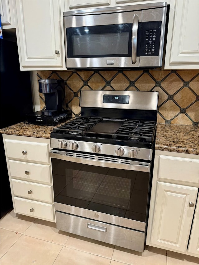 kitchen with dark stone countertops, decorative backsplash, light tile patterned floors, and appliances with stainless steel finishes