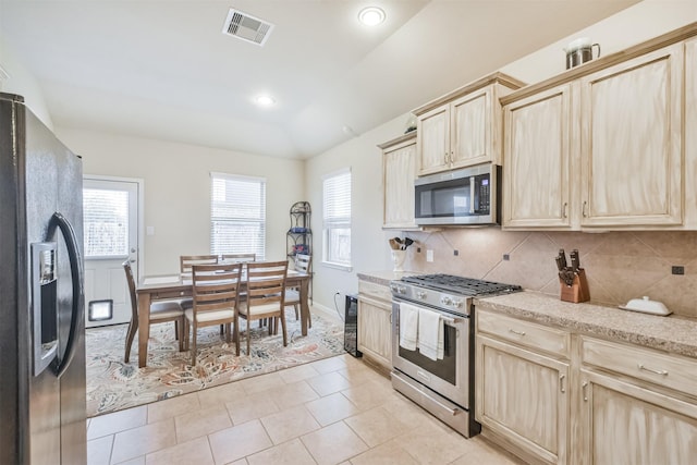 kitchen with appliances with stainless steel finishes, light brown cabinetry, tasteful backsplash, vaulted ceiling, and light tile patterned floors