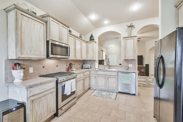 kitchen featuring sink, light brown cabinets, vaulted ceiling, decorative backsplash, and appliances with stainless steel finishes