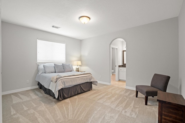 bedroom featuring a textured ceiling, light carpet, and connected bathroom