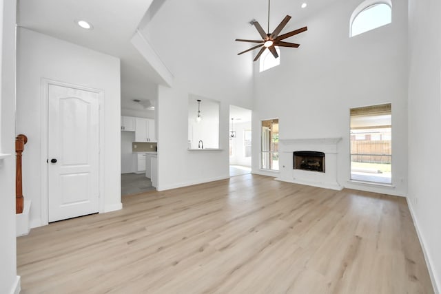 unfurnished living room with a towering ceiling, light hardwood / wood-style floors, and ceiling fan