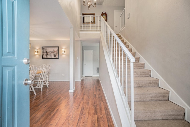 staircase featuring wood-type flooring, a high ceiling, and a chandelier