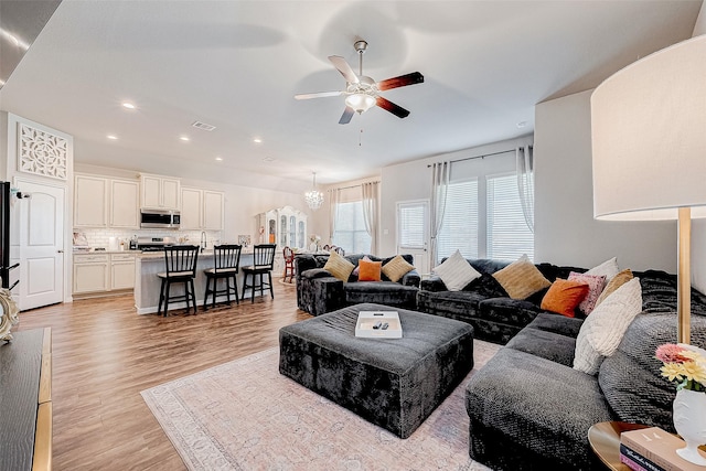 living room featuring ceiling fan with notable chandelier and light hardwood / wood-style flooring