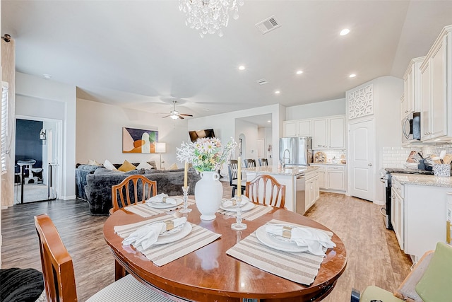 dining area featuring ceiling fan with notable chandelier, light wood-type flooring, and sink