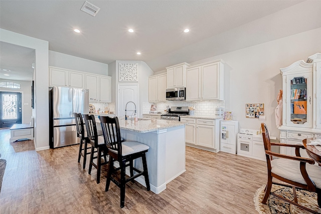 kitchen featuring light stone countertops, appliances with stainless steel finishes, tasteful backsplash, a kitchen island with sink, and white cabinets