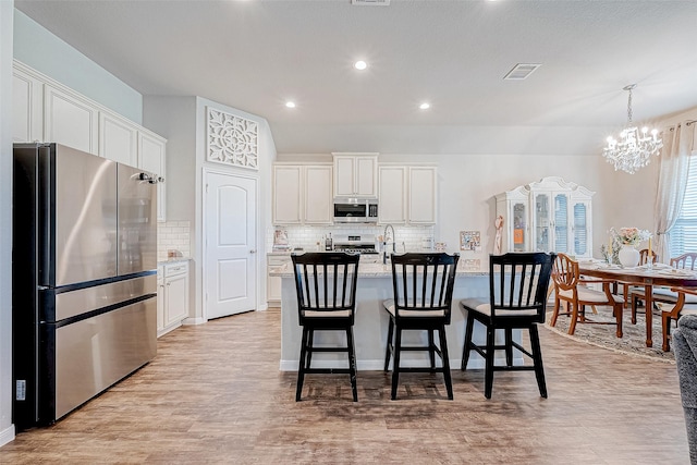 kitchen featuring tasteful backsplash, white cabinetry, an island with sink, and appliances with stainless steel finishes