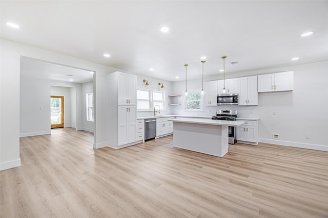 kitchen with stainless steel appliances, a kitchen island, light hardwood / wood-style flooring, white cabinetry, and hanging light fixtures