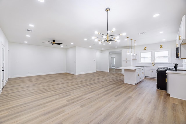 kitchen with white cabinets, a center island, ceiling fan with notable chandelier, and hanging light fixtures