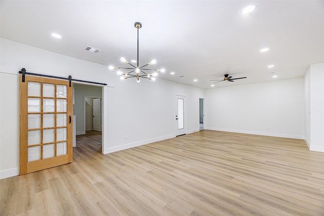 empty room featuring ceiling fan with notable chandelier, a barn door, and light hardwood / wood-style floors