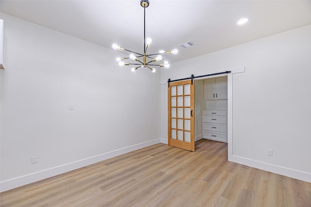 spare room with a notable chandelier, a barn door, and light hardwood / wood-style flooring