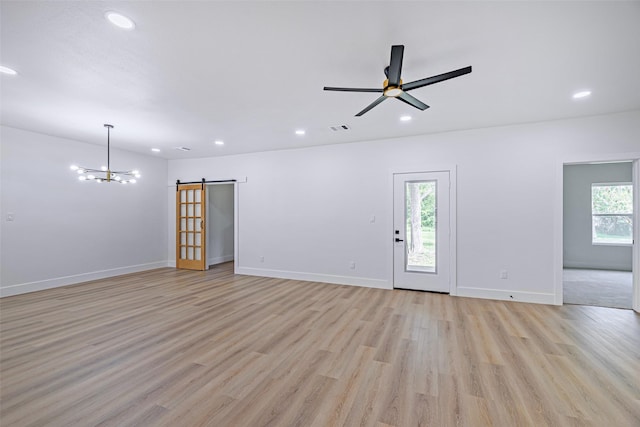 unfurnished living room with a barn door, light hardwood / wood-style flooring, and ceiling fan with notable chandelier