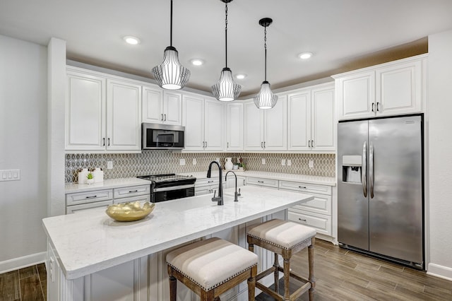 kitchen with an island with sink, appliances with stainless steel finishes, decorative light fixtures, light stone counters, and white cabinetry