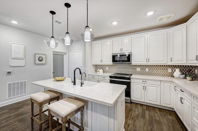 kitchen with dark hardwood / wood-style flooring, stainless steel appliances, a kitchen island with sink, decorative light fixtures, and white cabinets