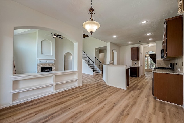 kitchen with decorative backsplash, light stone counters, hanging light fixtures, and a stone fireplace