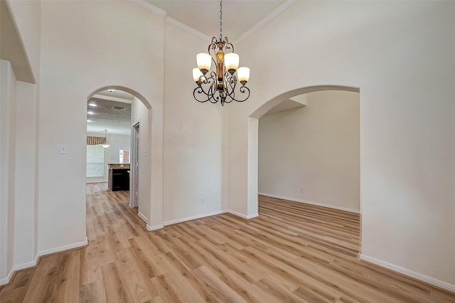 unfurnished room featuring light hardwood / wood-style flooring, a towering ceiling, a chandelier, and ornamental molding