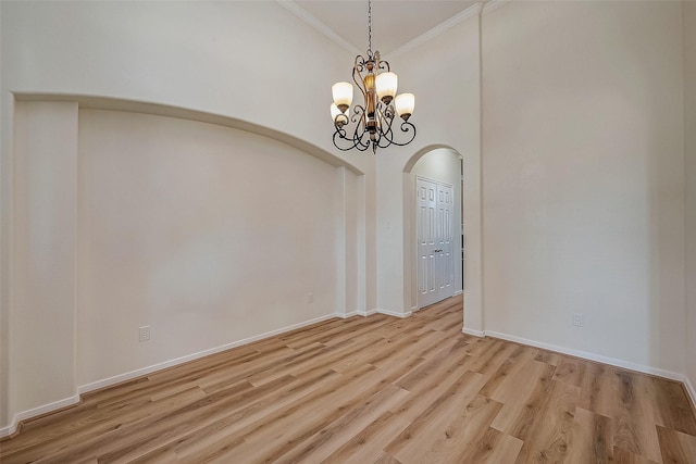 empty room with a notable chandelier, light wood-type flooring, ornamental molding, and a towering ceiling