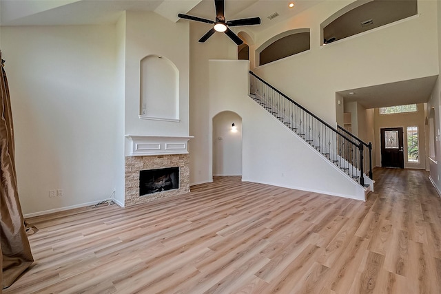 unfurnished living room featuring a high ceiling, light hardwood / wood-style floors, a stone fireplace, and ceiling fan