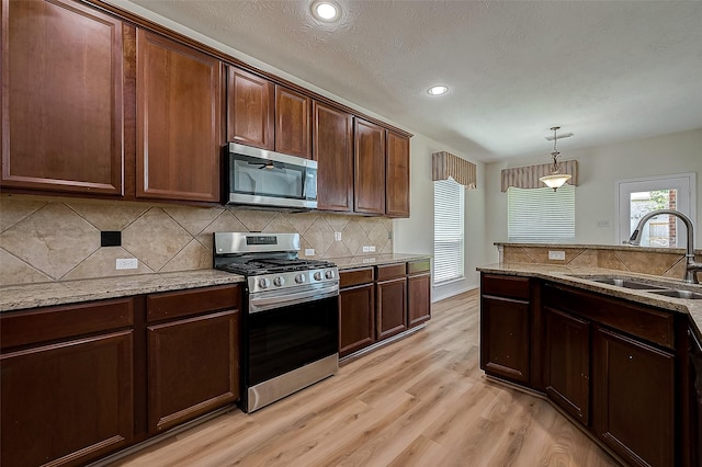 kitchen featuring sink, light hardwood / wood-style flooring, decorative light fixtures, decorative backsplash, and appliances with stainless steel finishes