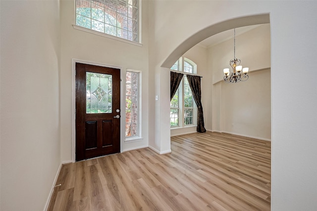 foyer featuring light wood-type flooring, a towering ceiling, and an inviting chandelier