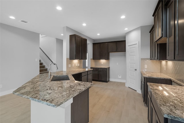 kitchen featuring light stone countertops, kitchen peninsula, backsplash, sink, and light hardwood / wood-style flooring