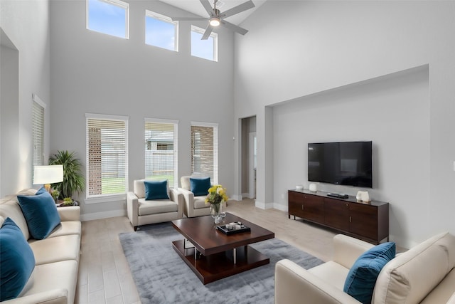 living room with ceiling fan, a high ceiling, and light wood-type flooring