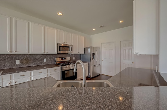 kitchen with white cabinetry, sink, backsplash, dark stone countertops, and appliances with stainless steel finishes