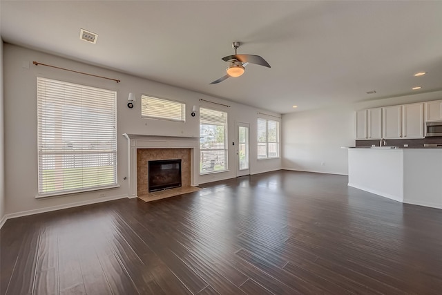 unfurnished living room with ceiling fan, a premium fireplace, and dark wood-type flooring