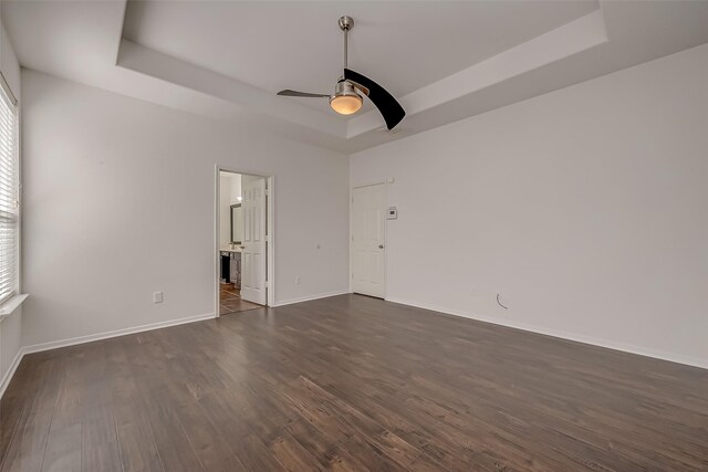 empty room with a raised ceiling, ceiling fan, and dark wood-type flooring