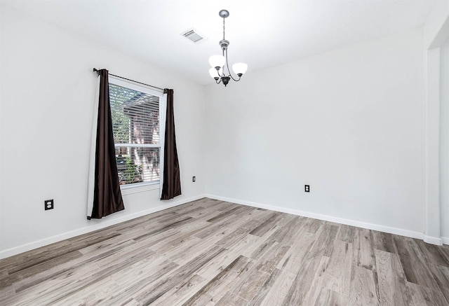 empty room featuring a chandelier and light wood-type flooring