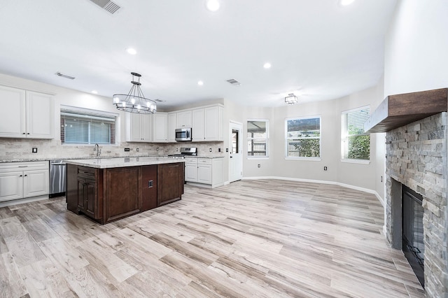 kitchen featuring hanging light fixtures, a stone fireplace, appliances with stainless steel finishes, white cabinets, and light wood-type flooring