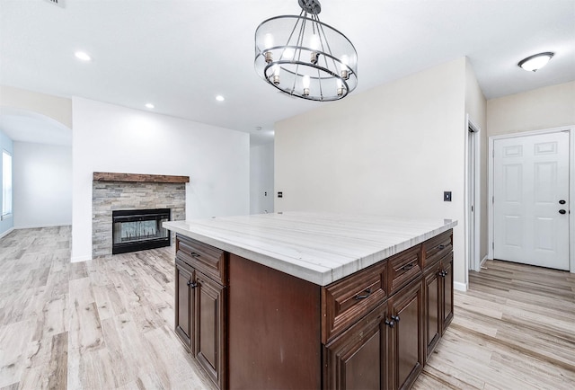 kitchen with light wood-type flooring, decorative light fixtures, a notable chandelier, a kitchen island, and a stone fireplace