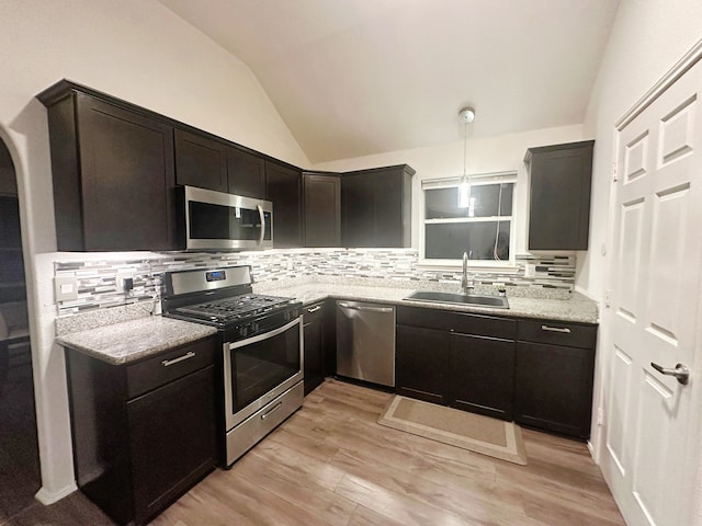 kitchen with light stone countertops, appliances with stainless steel finishes, backsplash, vaulted ceiling, and sink