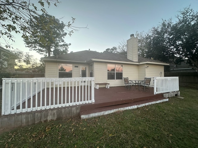 back house at dusk featuring a lawn and a wooden deck