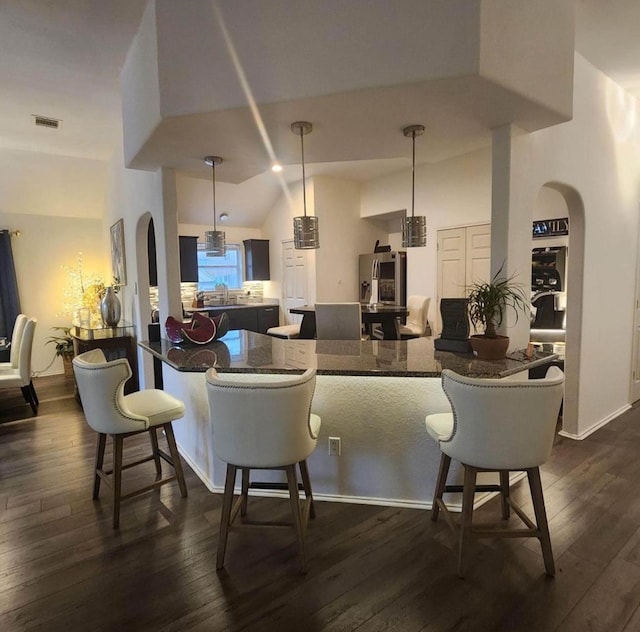 bar with dark stone counters, decorative light fixtures, vaulted ceiling, and dark wood-type flooring