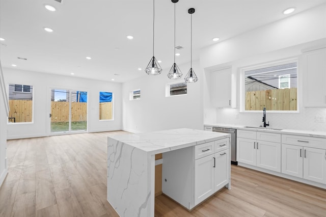 kitchen with white cabinetry, sink, a center island, stainless steel dishwasher, and decorative backsplash