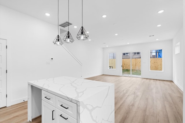 kitchen with light stone countertops, hanging light fixtures, a kitchen island, light hardwood / wood-style floors, and white cabinets