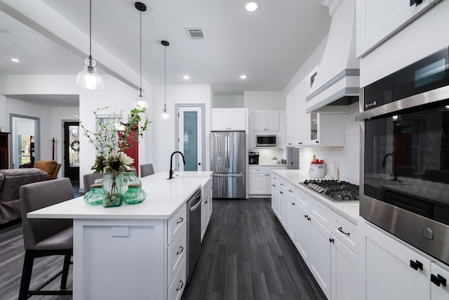 kitchen featuring a kitchen breakfast bar, stainless steel appliances, a kitchen island with sink, white cabinets, and hanging light fixtures