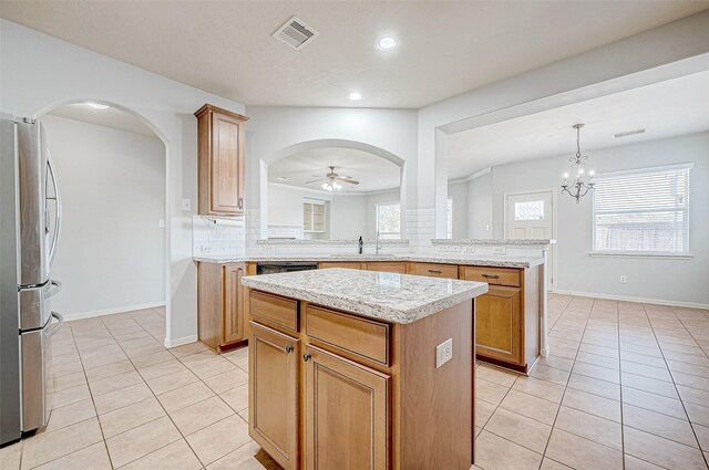 kitchen with a center island, hanging light fixtures, light tile patterned floors, stainless steel refrigerator, and kitchen peninsula