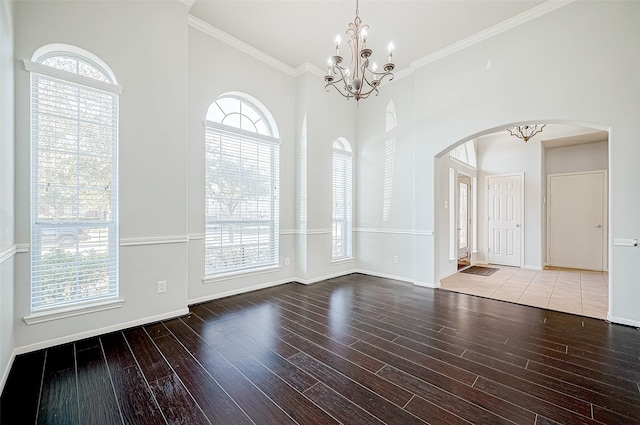 spare room with a high ceiling, wood-type flooring, ornamental molding, and a notable chandelier