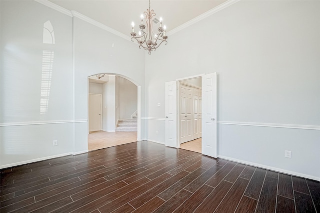 empty room featuring an inviting chandelier, a towering ceiling, ornamental molding, and hardwood / wood-style floors