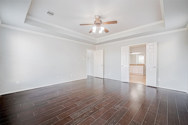 unfurnished bedroom with crown molding, ensuite bath, a tray ceiling, and dark hardwood / wood-style flooring