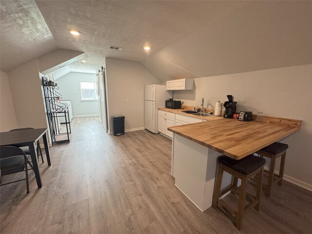 kitchen with wood counters, lofted ceiling, white refrigerator, a textured ceiling, and a breakfast bar area