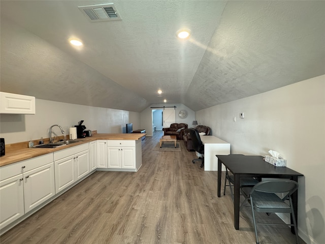 kitchen featuring sink, butcher block countertops, light hardwood / wood-style floors, lofted ceiling, and white cabinets