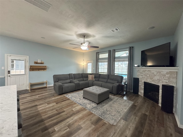 living room featuring a stone fireplace, ceiling fan, dark hardwood / wood-style flooring, and a textured ceiling