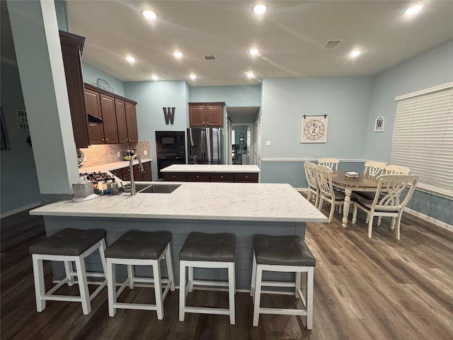 kitchen featuring sink, dark wood-type flooring, backsplash, kitchen peninsula, and black appliances