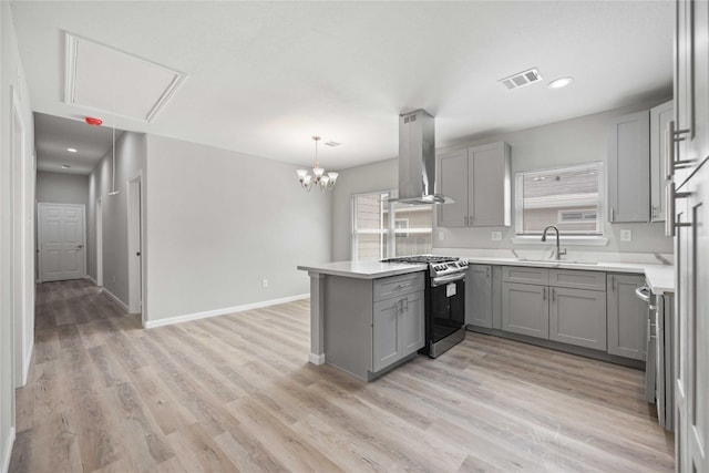 kitchen with gray cabinetry, wall chimney range hood, stainless steel gas range, kitchen peninsula, and decorative light fixtures