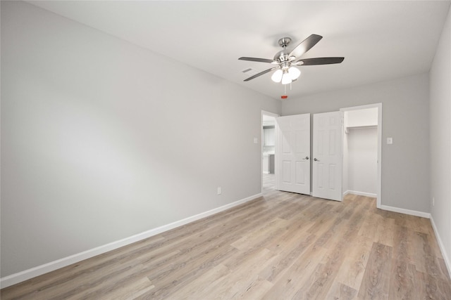 unfurnished bedroom with ceiling fan, light hardwood / wood-style floors, a walk in closet, and a closet