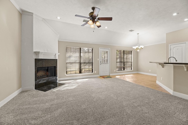 unfurnished living room with crown molding, a textured ceiling, light carpet, a fireplace, and ceiling fan with notable chandelier